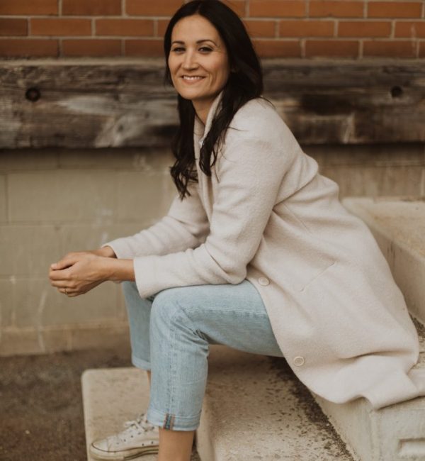 Emily Cassolato, Guelph realtor, sits on concrete stairs outdoors smiling into the camera.